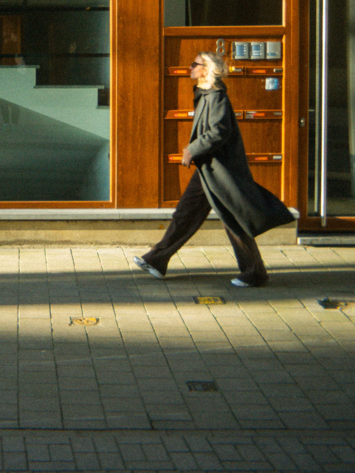 A woman in a long coat walking past a shopfront in late afternoon light