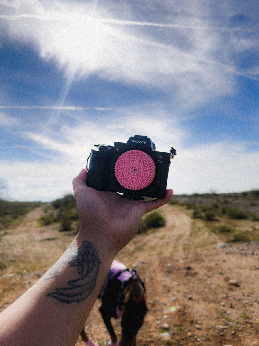 A Sony camera with the Retropia Pink Edition lens held up against a desert sky