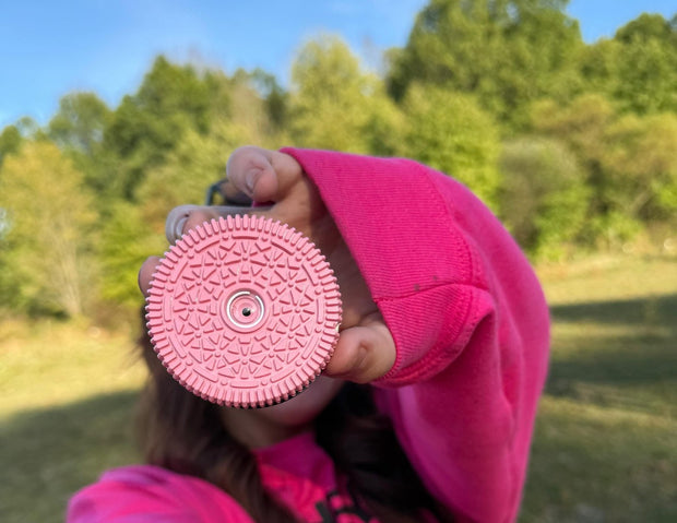 Someone in a bright pink hoodie holding the Retropia Pink Edition lens up to the camera